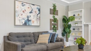 A living room with a grey sofa, a round wooden coffee table, and a large abstract painting on the wall. - Old Town Monrovia Hot Tub Retreat (Monrovia)
