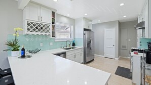 A modern kitchen with white cabinetry, a stainless steel refrigerator, and a large island with a sink. - Old Town Monrovia Hot Tub Retreat (Monrovia)