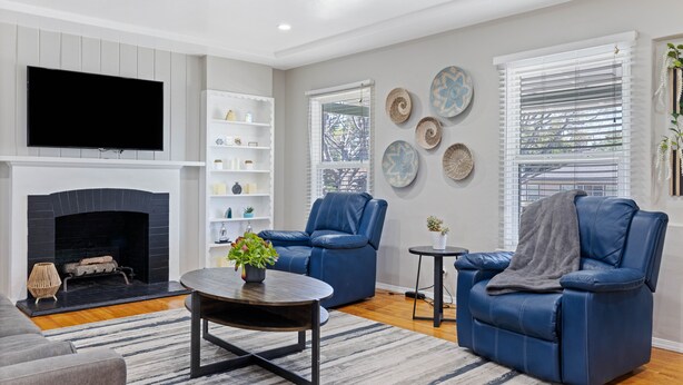 A living room with a fireplace, two blue leather chairs, a coffee table, and decorative plates on the wall. - Old Town Monrovia Hot Tub Retreat (Monrovia)