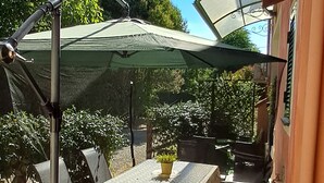 Eine Terrasse im Freien mit Tisch und Stühlen, einem grünen Sonnenschirm und einer Metallkonstruktion.
