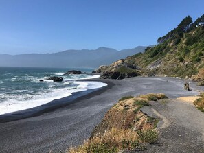 Una carretera costera con una playa a un lado y un promontorio boscoso al otro.