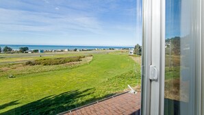 A view from a window overlooking a grassy field with a clear sky. - Cozy Oceanview Hideaway#2 on Golf Course/Airport (Whitethorn)