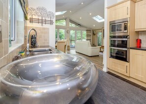 A modern kitchen with a large stainless steel hot tub, a built-in oven, and a dining area with a view of the outdoors.