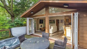 Een terras buiten met een hottub, rieten meubels en een glazen deur naar een woonruimte.