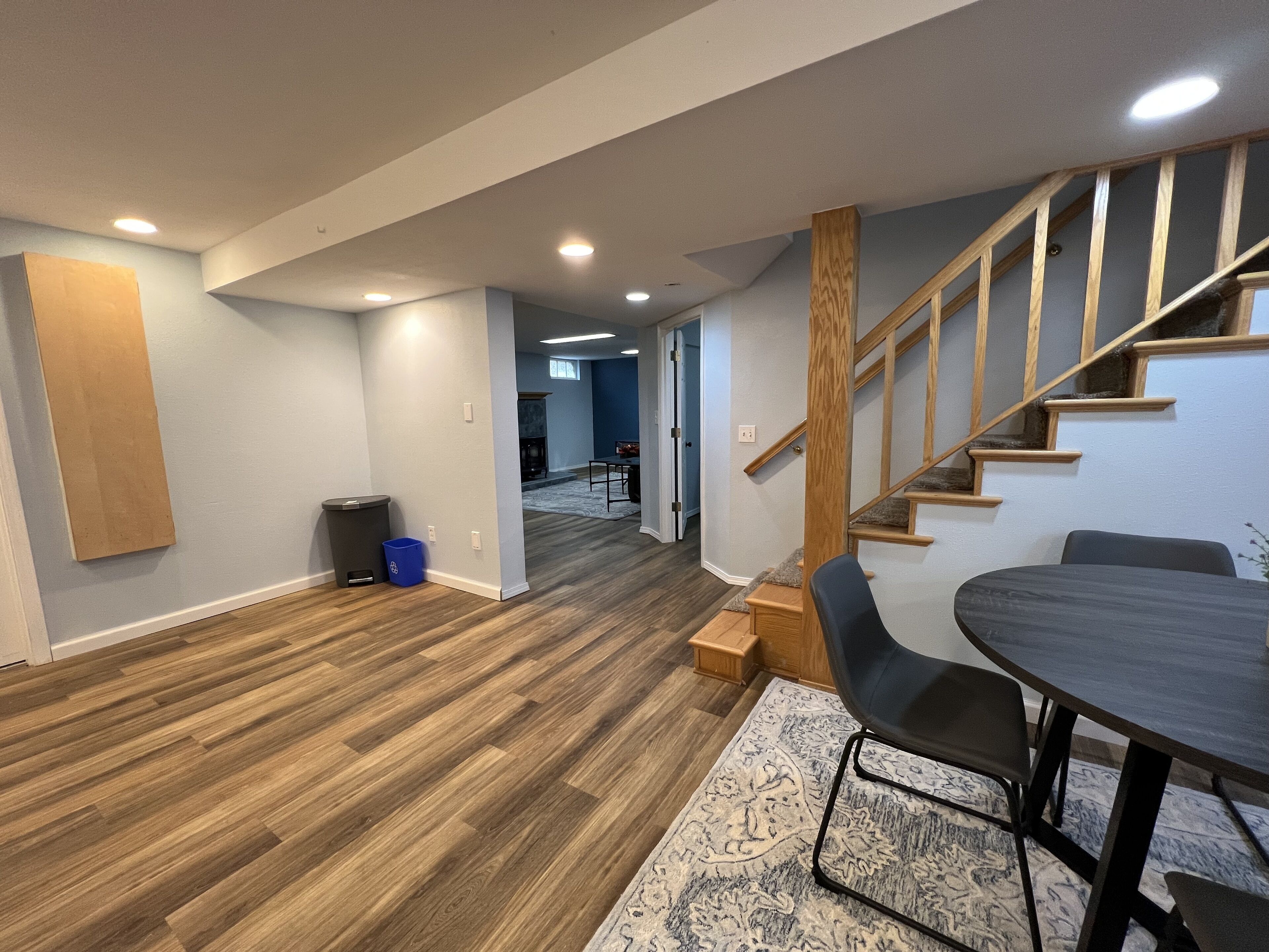 A spacious living area with a wooden staircase, a dining table with chairs, and a rug on the floor.