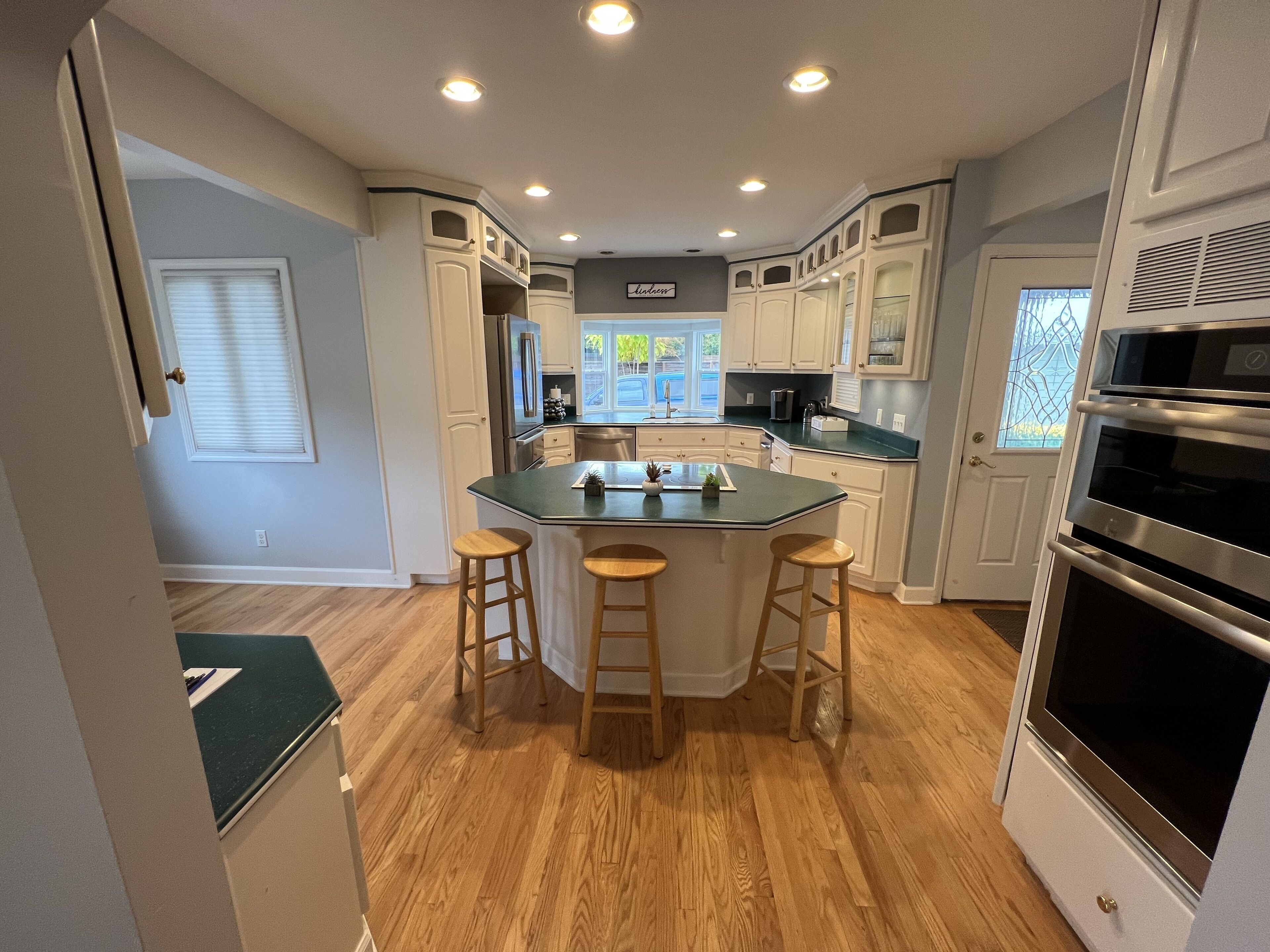 A modern kitchen with a central island, wooden stools, stainless steel appliances, and white cabinetry.