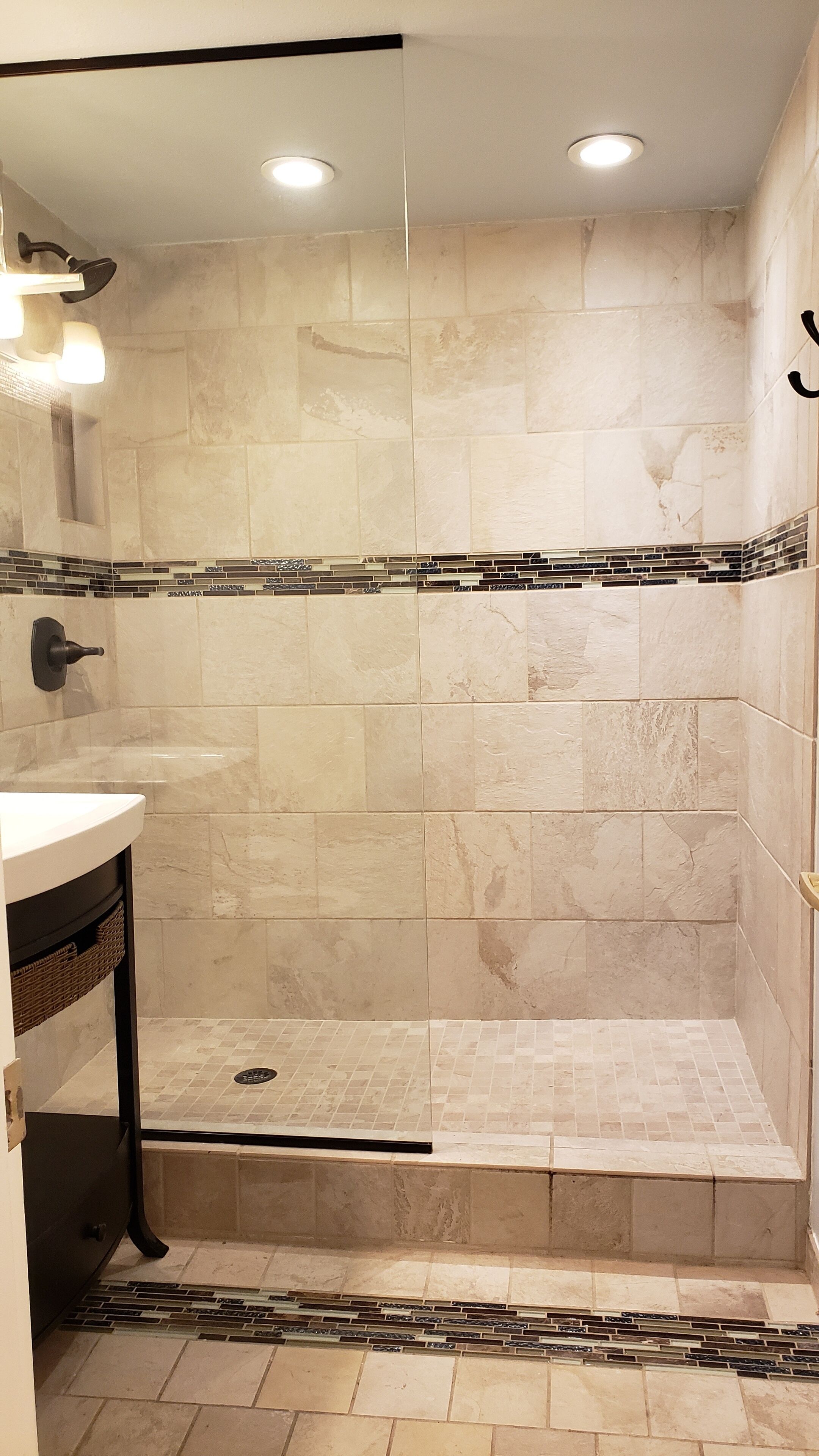 Un espacio de ducha con azulejos color beige, una puerta de vidrio y suelo de cerámica.