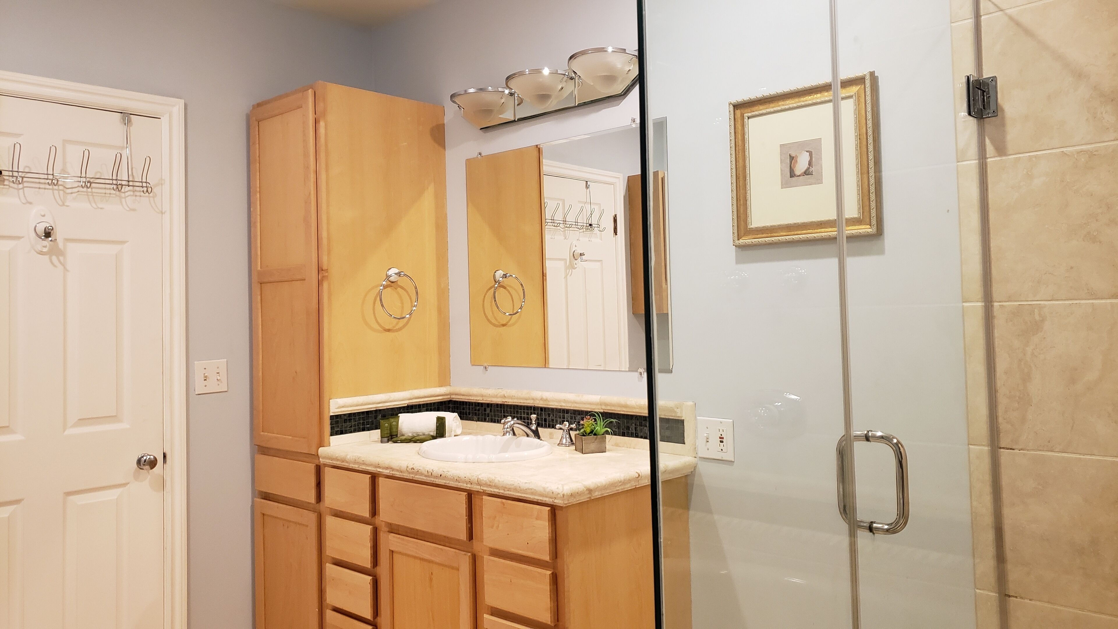 Une salle de bain avec des meubles en bois, un lavabo, un miroir et un espace douche.