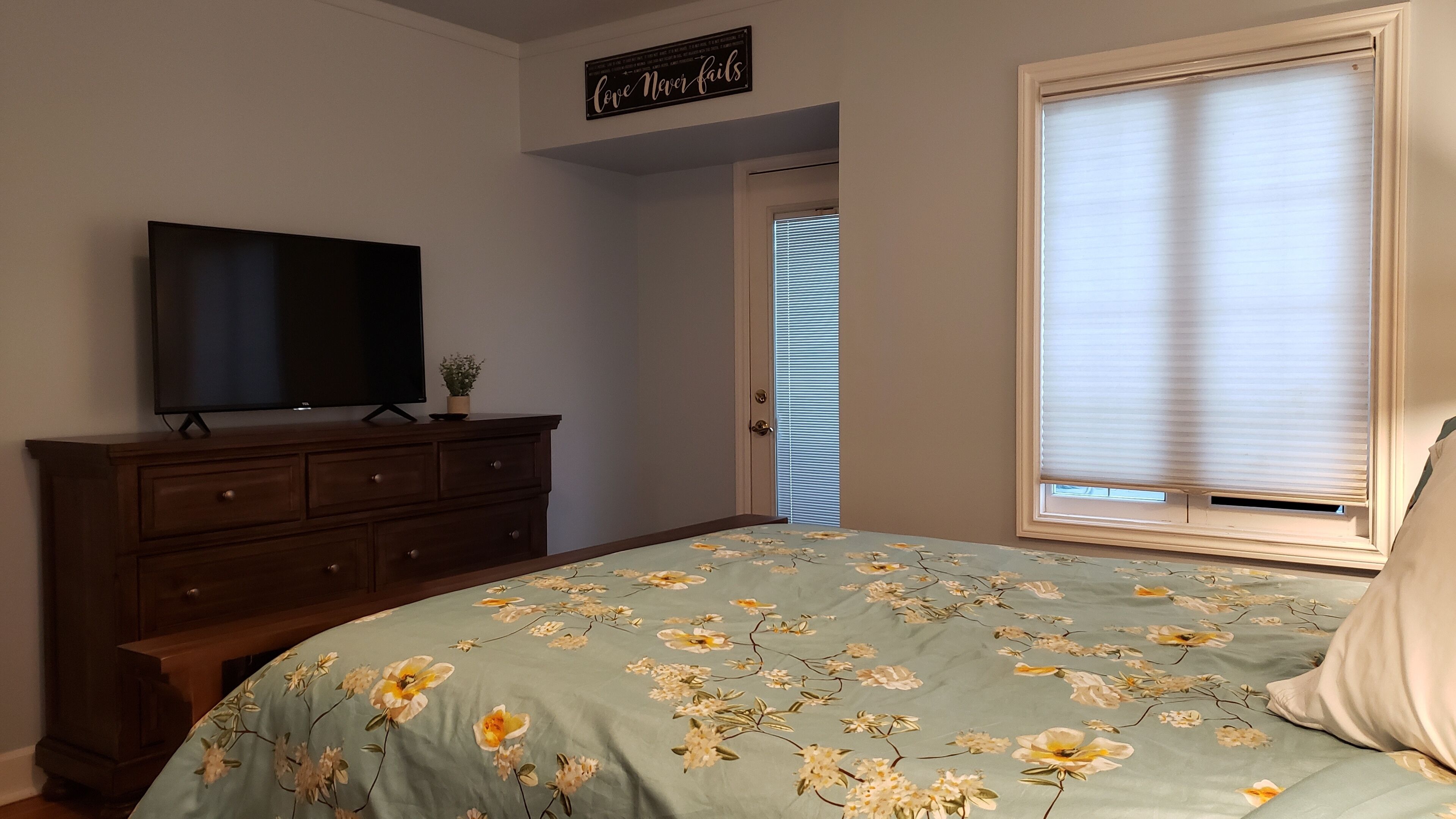 A bedroom with a bed, a dresser, a television, and a window with blinds.