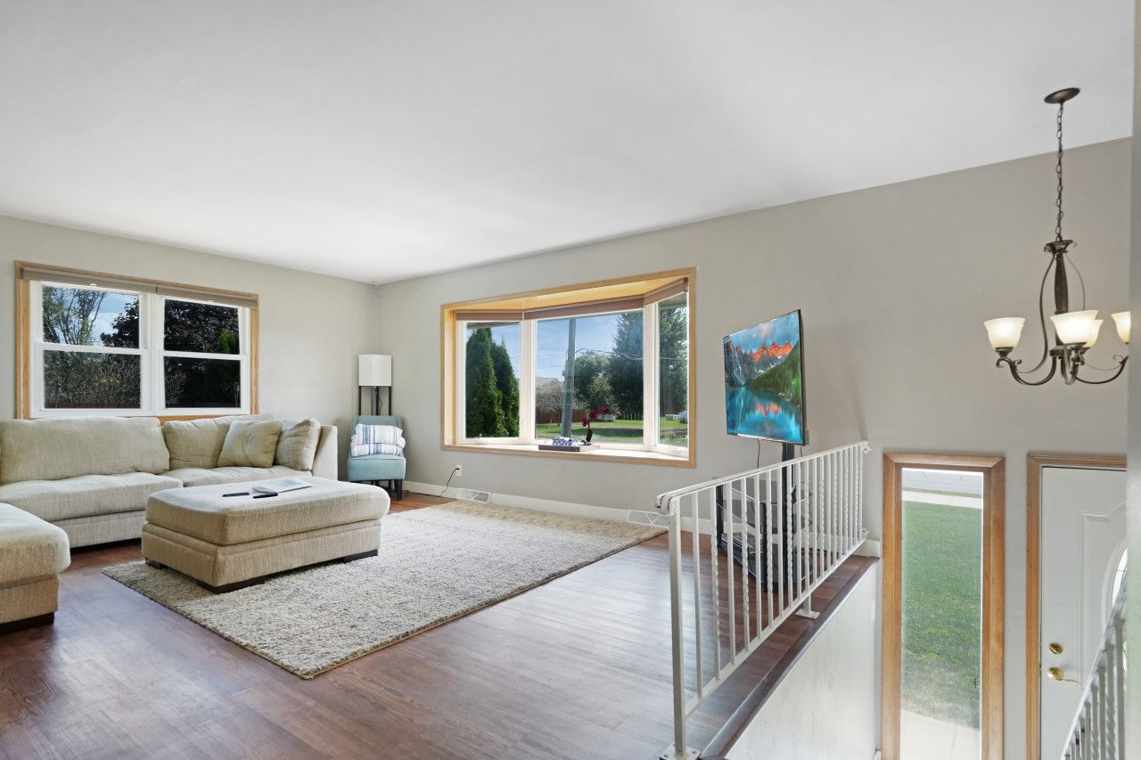 A spacious living room with a large sectional sofa, a small ottoman, and a view of a garden through large windows.