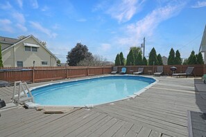 A wooden deck with a swimming pool, lounge chairs, and a wooden fence.