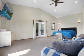 A bedroom with a bed, a ceiling fan, a TV, and a window with curtains.