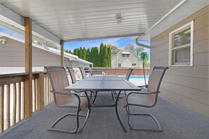 A covered patio with a table and chairs, a pool in the background, and a wooden deck.