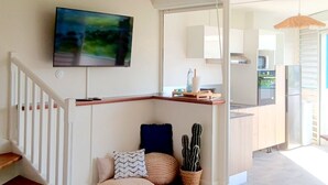 A modern kitchen with a built-in oven, a refrigerator, and a microwave. There is a dining area with a table and chairs, and a large window providing natural light. - Les Parasols Suite Prestige • RelaXMooD signature (Le Diamant)