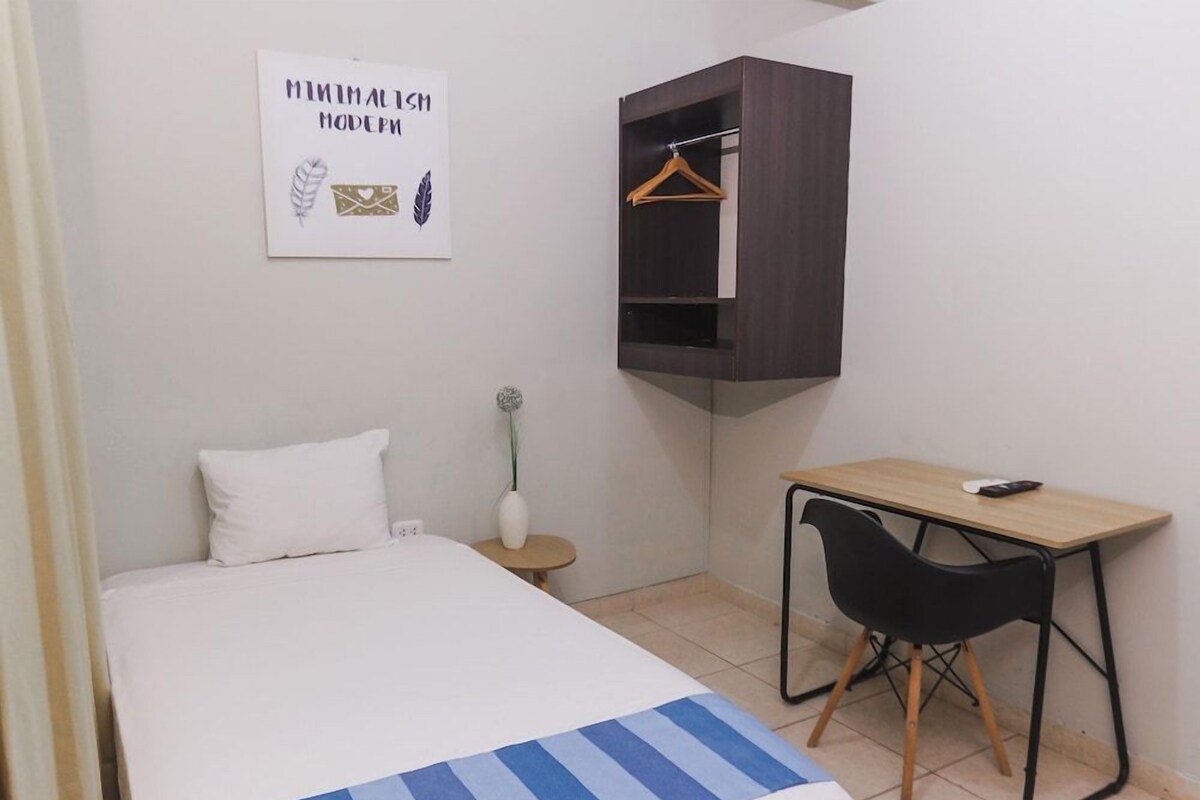 Une chambre à coucher comprenant un lit, un bureau, une chaise, une armoire suspendue, une petite table avec un vase et un élément de décoration murale.