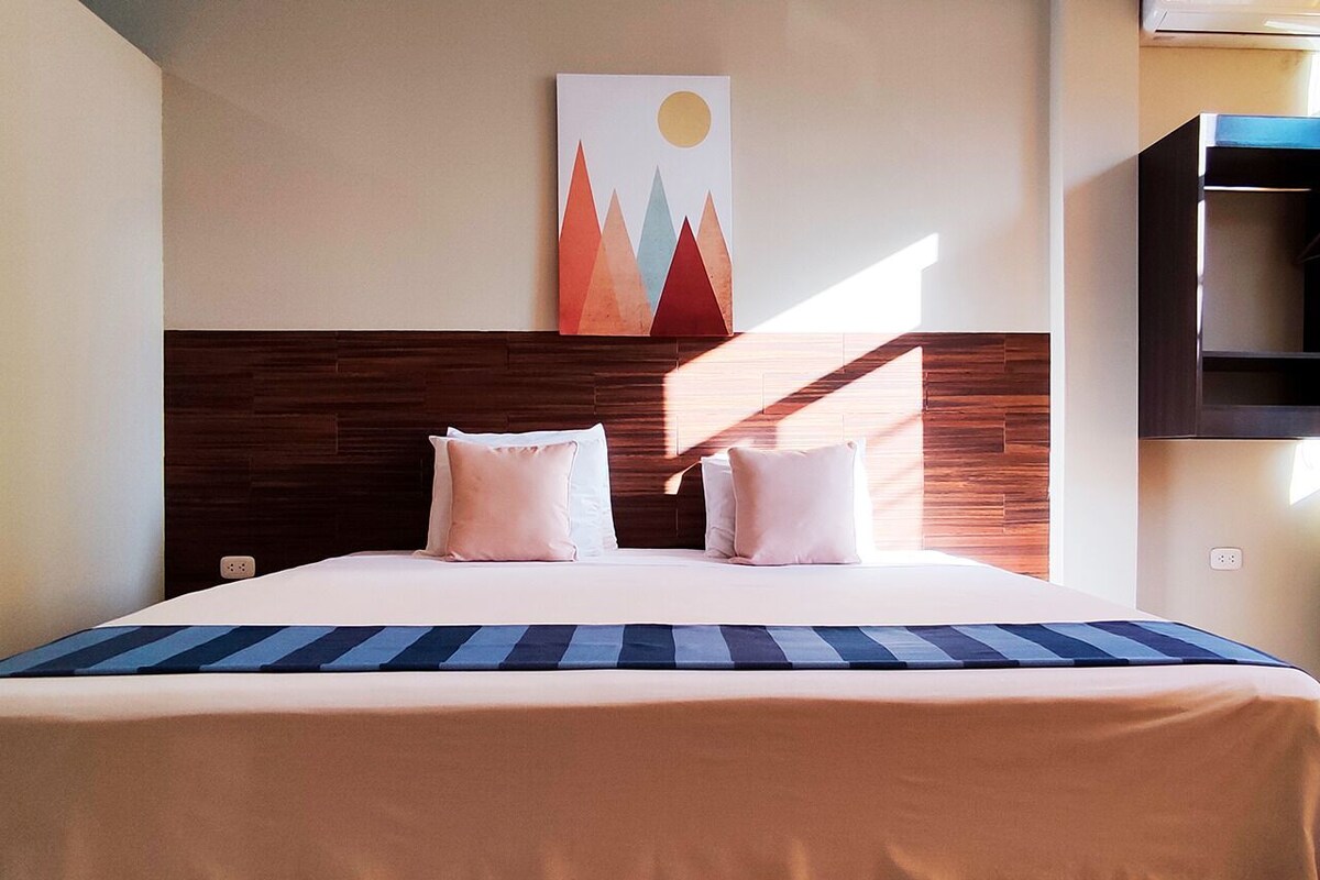 Une chambre d’hôtel avec un lit, des oreillers, une tête de lit en bois, une œuvre d’art accrochée au mur et un téléviseur.