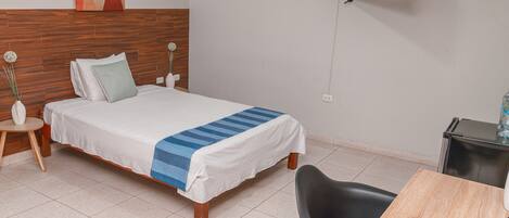 Una habitación de hotel con una cama, un escritorio con una silla, un televisor y un televisor montado en la pared.