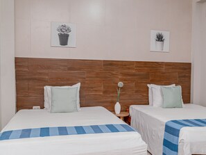 Habitación de hotel con dos camas, un cabecero de madera y dos plantas en macetas colgando de la pared.