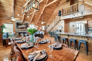 A spacious dining area with a wooden table set for a meal, a kitchen with modern appliances, and a staircase leading to an upper level.