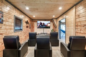 A wooden cabin interior with a TV, black leather chairs, and a staircase.