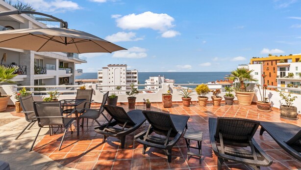 A terrace with outdoor seating, potted plants, and a view of the sea.