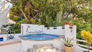 A hot tub surrounded by lush greenery, a stone bench, and a potted plant.