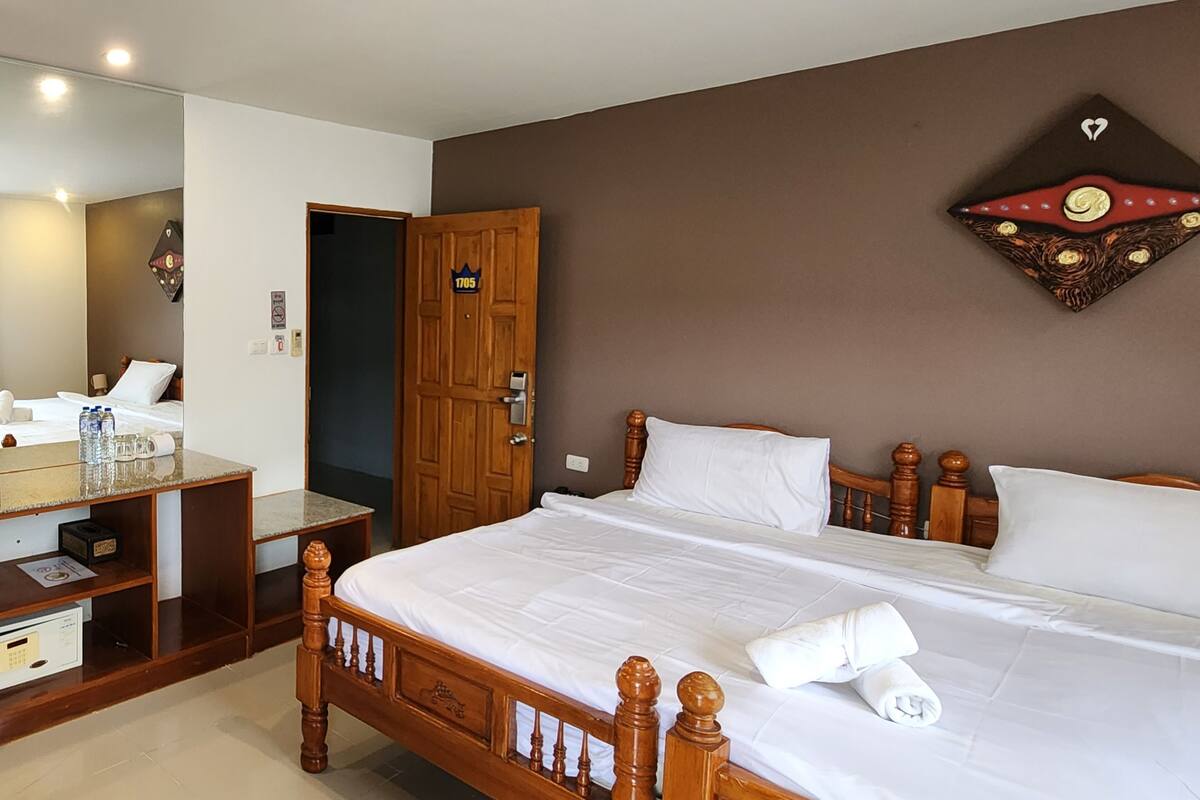 Ein Hotelzimmer mit einem hölzernen Bett, einem Schreibtisch mit Spiegel, einem Kleiderschrank und einem an der Wand hängenden Kunstwerk.