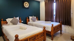 Ein Hotelzimmer mit zwei Holzbett, einer dunkel-blaugrünen Akzentwand und einem Fenster mit braunen Vorhängen.