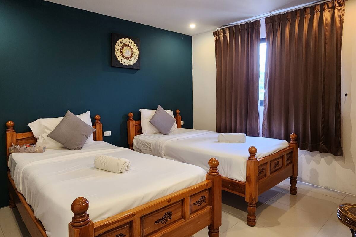 Ein Hotelzimmer mit zwei Holzbett, einer dunkel-blaugrünen Akzentwand und einem Fenster mit braunen Vorhängen.