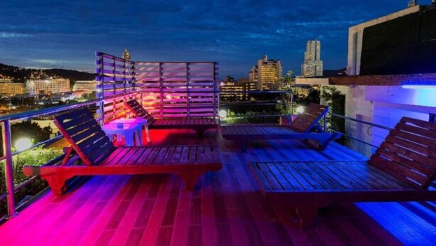 Eine Dachterrasse mit Holzliegen und einem kleinen Tisch mit Blick auf eine nächtliche Stadtlandschaft.