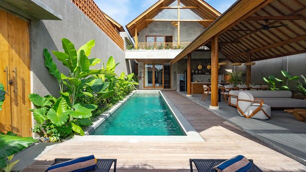 A modern pool area with a wooden deck, lounge chairs, and a covered seating area with a table and chairs. - Jiwoku Villas (Canggu)