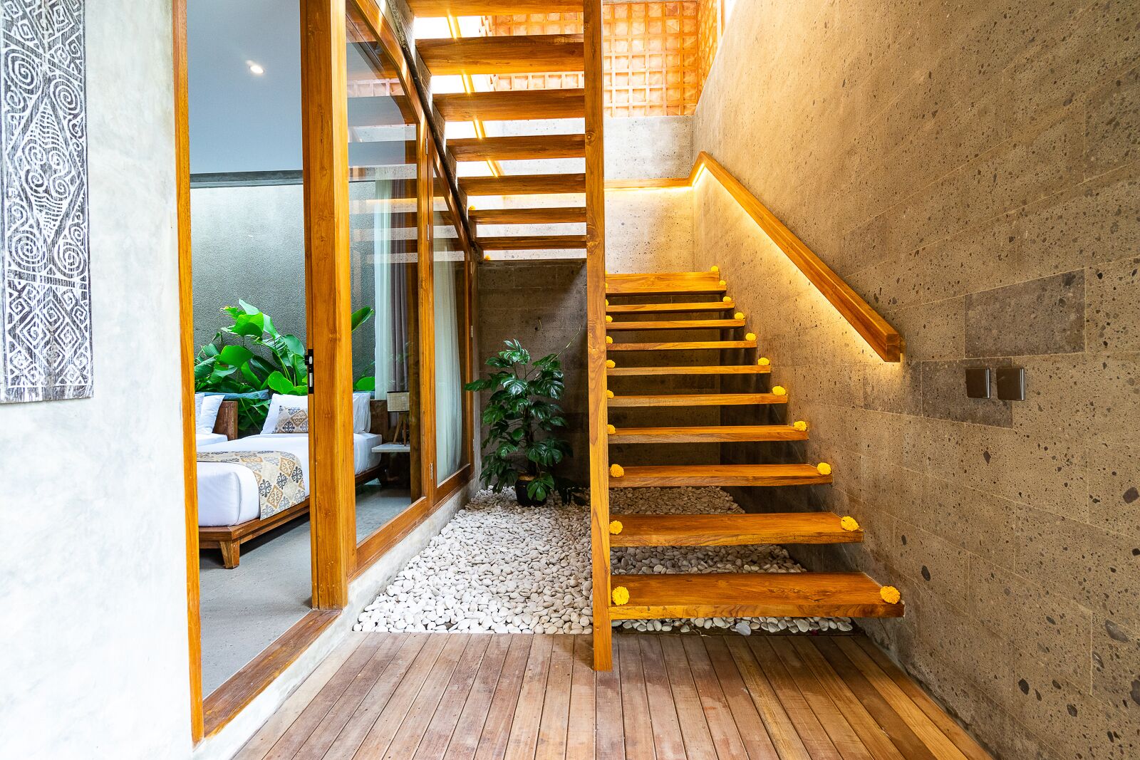 A wooden staircase with a handrail, leading to a room with a bed and a plant.