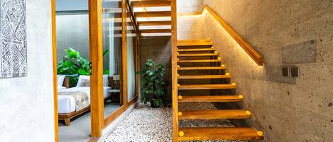 A wooden staircase with a handrail, leading to a room with a bed and a plant.
