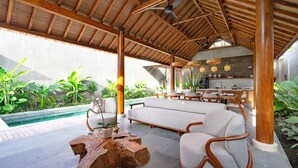 A spacious outdoor area with a pool, wooden furniture, and a kitchen in the background. - Jiwoku Villas (Canggu)