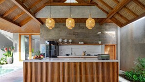 A modern kitchen with a wooden island, hanging wicker lights, and a concrete backsplash. - Jiwoku Villas (Canggu)