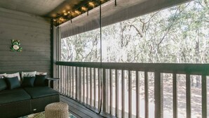 A covered outdoor seating area with a wooden bench, a wicker ottoman, and a sofa with cushions. - Queen Studio | Full Kitchen, Screened Balcony | 1 Small Dog | Ravines (Middleburg)
