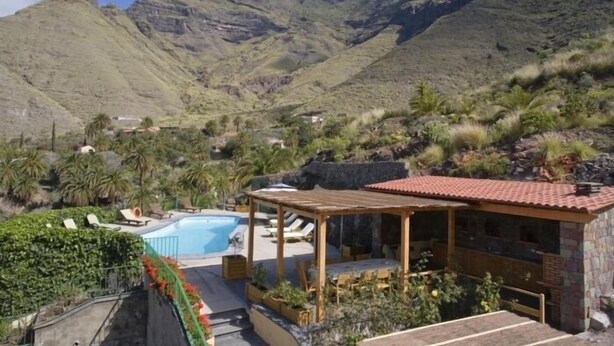 Un resort con piscina, mobiliario exterior y vistas a montañas.