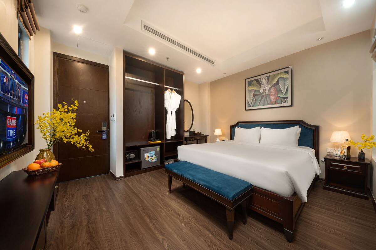 A hotel room with a large bed, a bench, a TV, a wardrobe, and a painting on the wall.