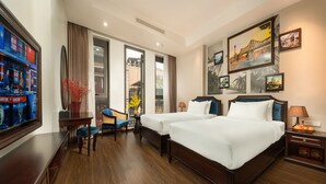A hotel room with two beds, a desk, a chair, a TV, and artwork on the walls. - Hanoi Fiesta Grand Hotel (Hanoi)