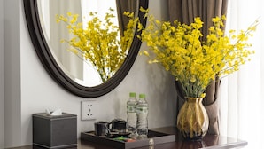 A wooden vanity with a mirror, a vase with yellow flowers, a tissue box, and a blue stool. - Hanoi Fiesta Grand Hotel (Hanoi)
