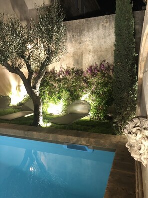 A pool with a clear blue water surface, surrounded by a garden with various plants and a stone bench. - Luxurious Bastide in the center of St Remy, quiet location, heated swimming pool (Saint-Rémy-de-Provence)