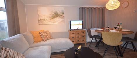 A modern living room with a sofa, a coffee table, and a dining area with chairs and a table set for two.