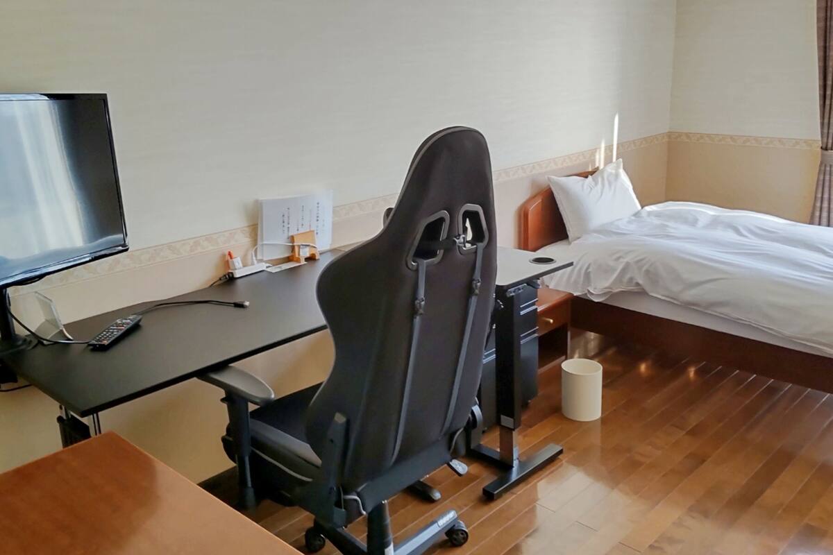 A hotel room with a bed, a desk with a chair, a television, and a remote control.