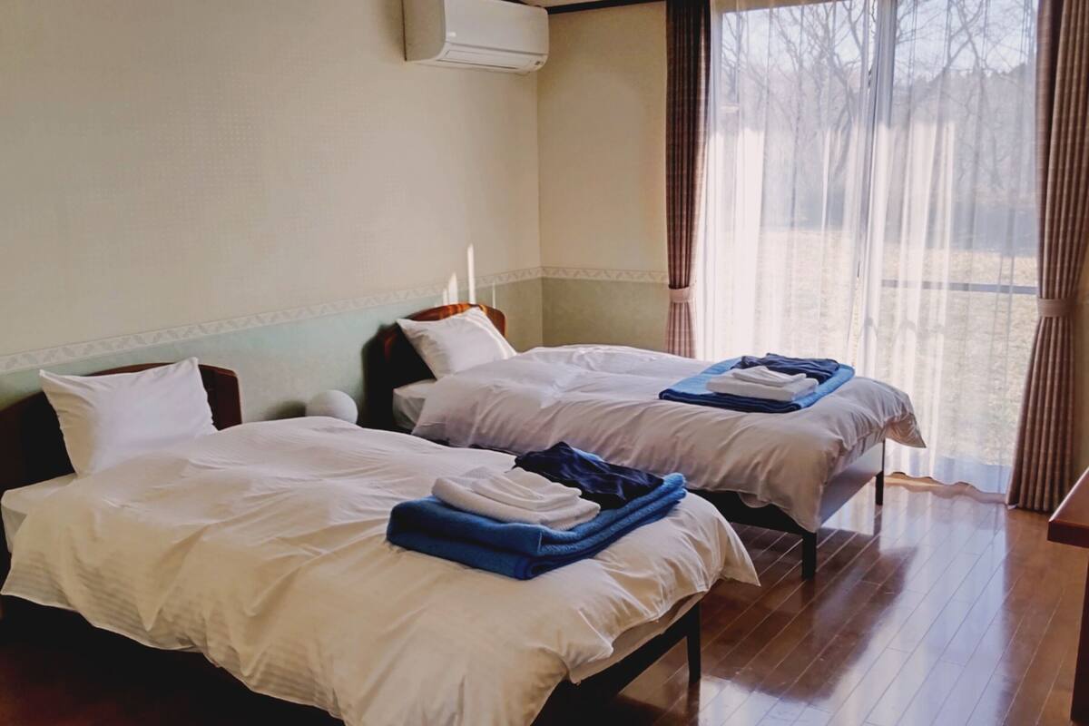 A hotel room with two beds, a window with curtains, and an air conditioning unit on the wall.