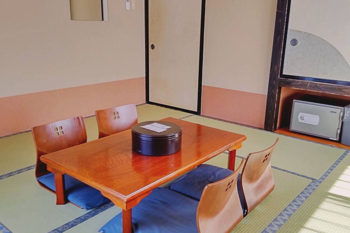 A traditional Japanese room with tatami mat flooring, a wooden table with cushions, and a sliding door.