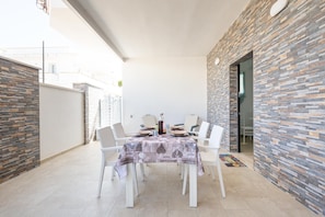 A dining area with a table set for four, surrounded by white chairs, against a wall with a patterned stone design.