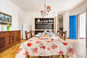 A dining area with a table set for four, a chandelier, and a kitchen in the background.