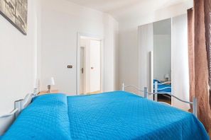 Un dormitorio con cama, mesita de noche, espejo y puerta que da a otra habitación.