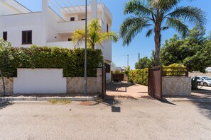 A modern white building with a stone base, surrounded by greenery and palm trees.