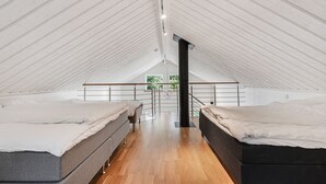 Een zolderkamer met hoge plafonds, twee bedden, houten vloeren en uitzicht op groen.
